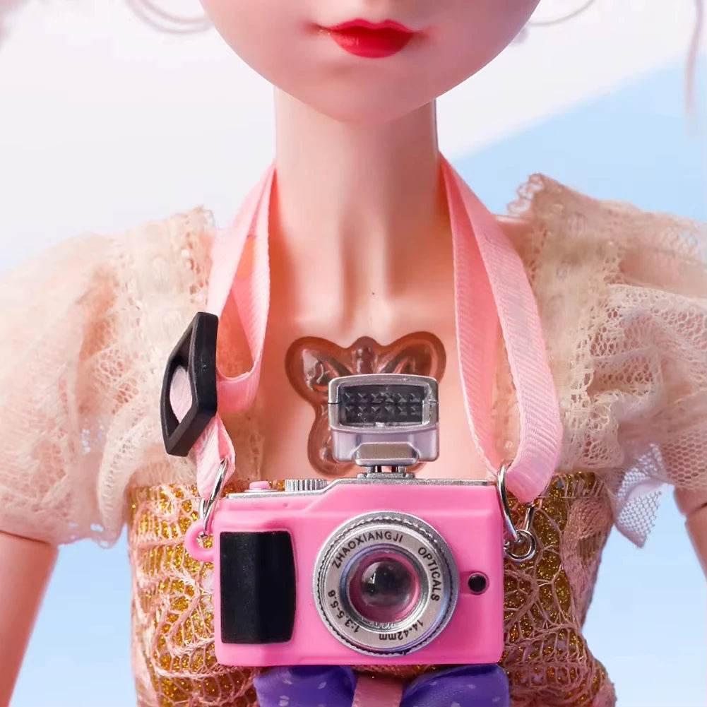 Pink vintage-style camera necklace with silver lens and black detailing on doll with lace dress.