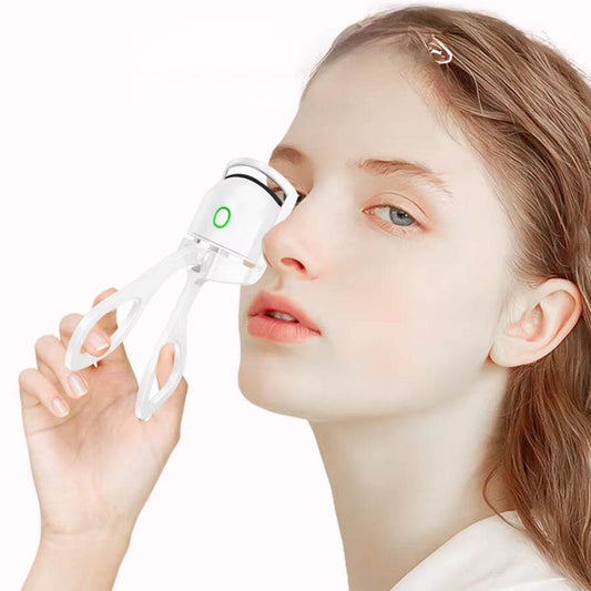 Mini pink rechargeable heated eyelash curler held near woman's eye with LED indicator light on.
