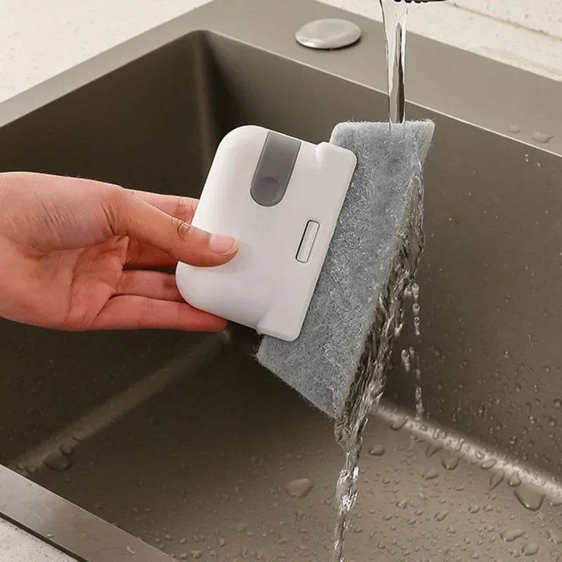 White handheld groove cleaning brush with gray scrubbing pad under running water above kitchen sink.