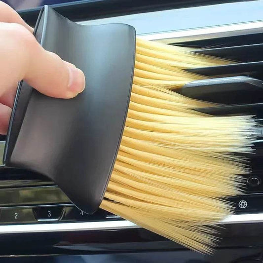 Black handheld dust brush with soft beige bristles cleaning car air conditioning vent slot.