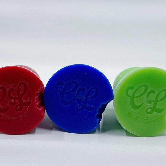 Red, blue, and green round Huckabuck candles with bite marks and embossed initials on a white background.