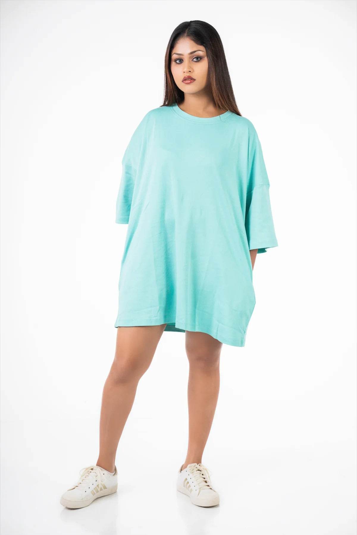 Woman wearing oversized light blue relaxed fit t-shirt with short sleeves and white sneakers.