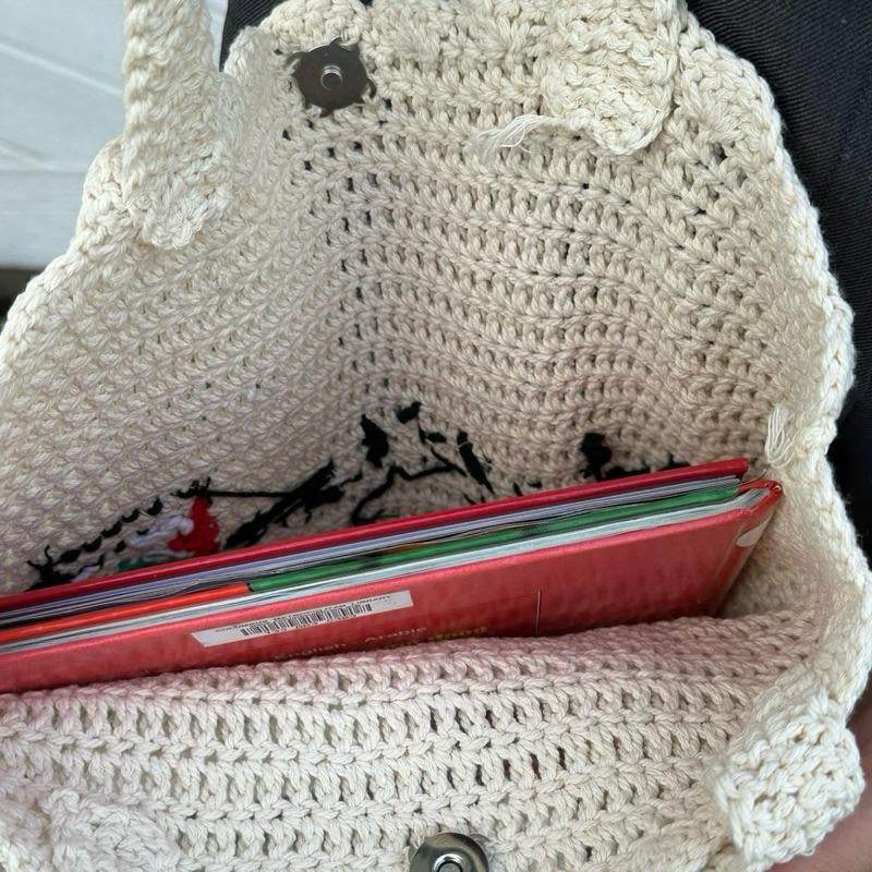 Cream-colored handmade crochet tote bag with open top holding colorful folders.