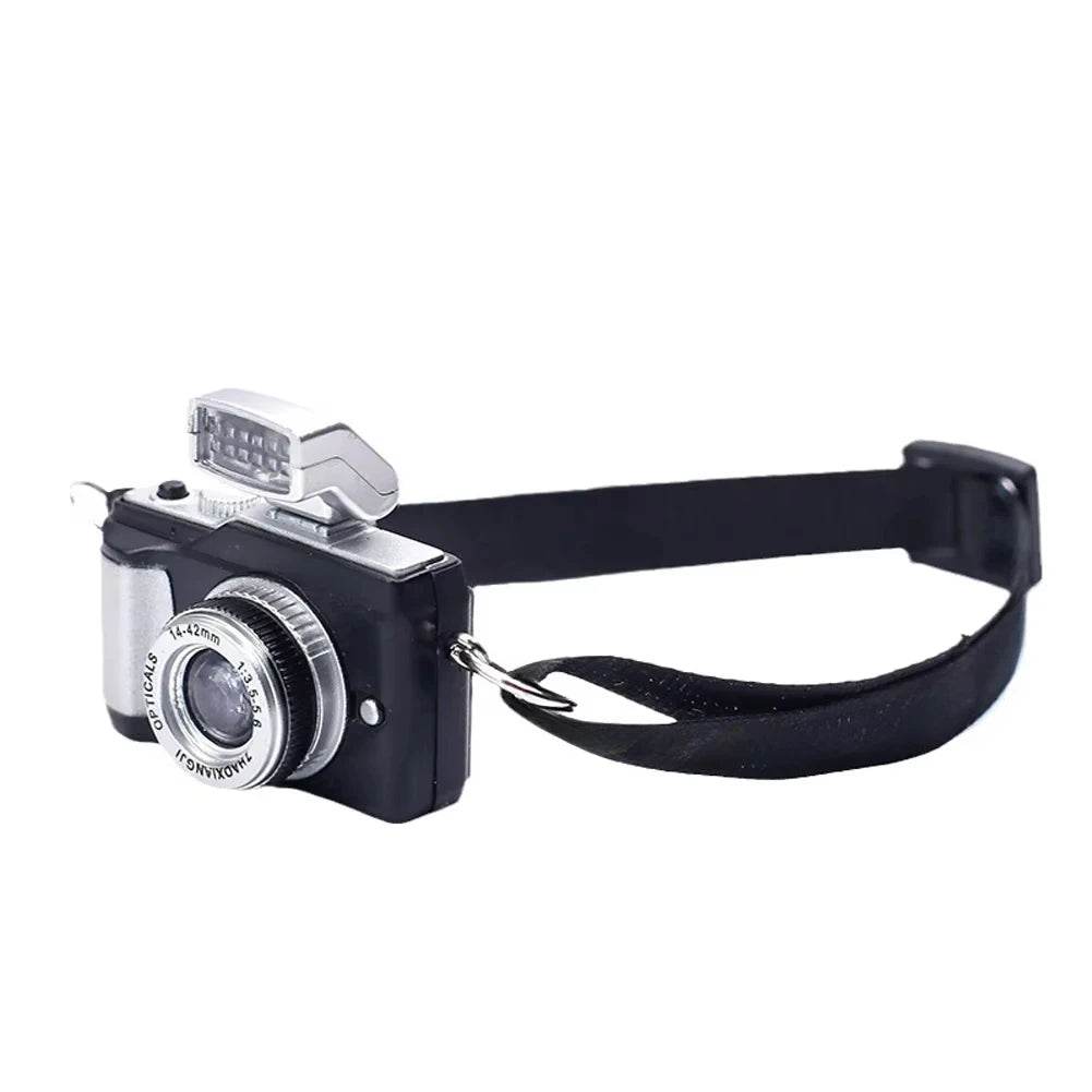 Miniature black and silver vintage-style camera with flash and adjustable black strap accessory.