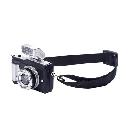 Miniature black and silver vintage-style camera with flash and adjustable black strap accessory.