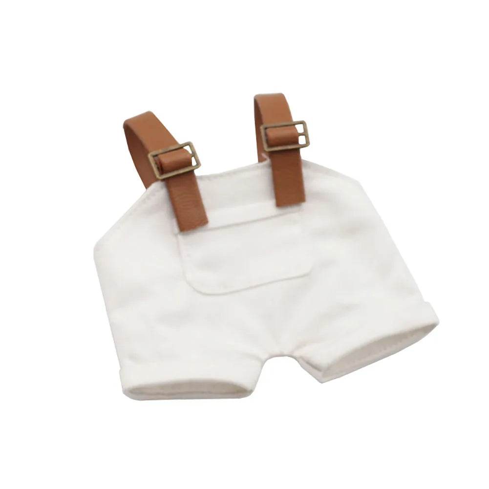 White cotton doll overalls with brown adjustable straps and front pocket detail.