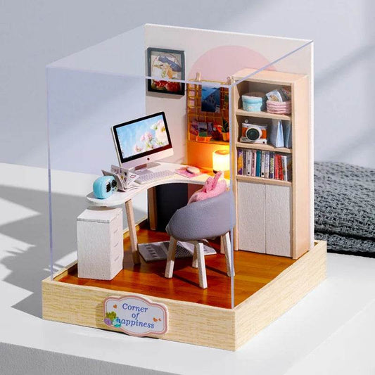 Miniature 3D dollhouse office corner with desk, computer, gray chair, bookshelf, and desk lamp on wooden floor.
