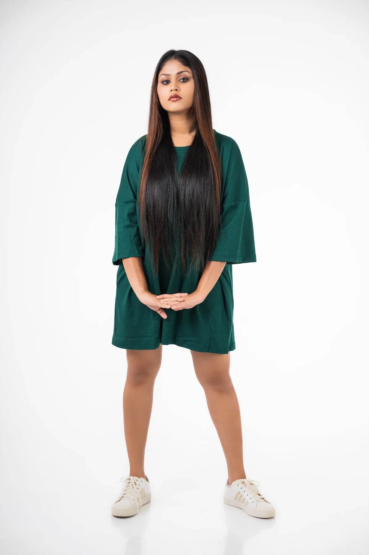 Woman wearing a dark green relaxed fit oversized t-shirt with mid-thigh length and white sneakers.