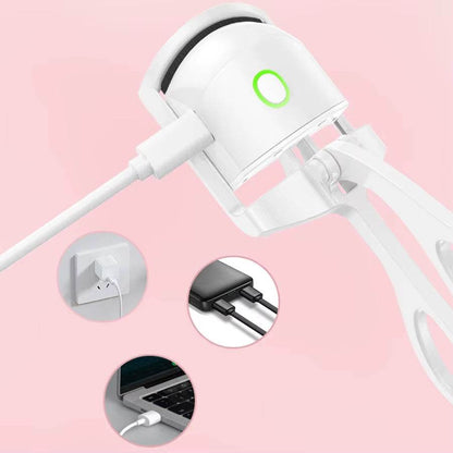 Mini white rechargeable heated eyelash curler with green power indicator and USB charging cable on pink background.