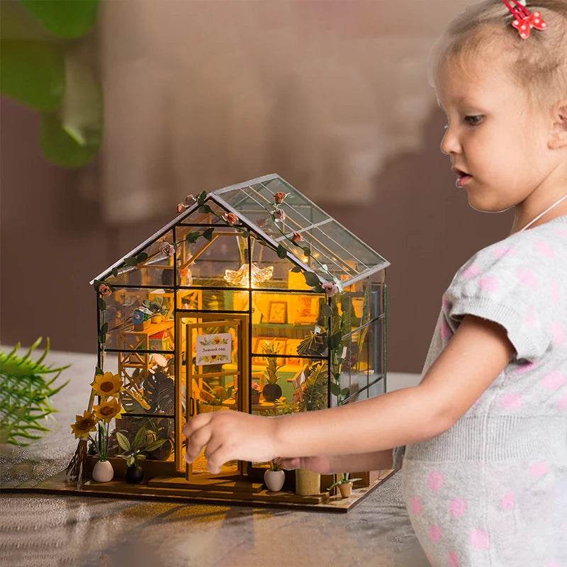 Miniature glass dollhouse with wooden frame, detailed furniture, sunflowers, and warm interior lighting.