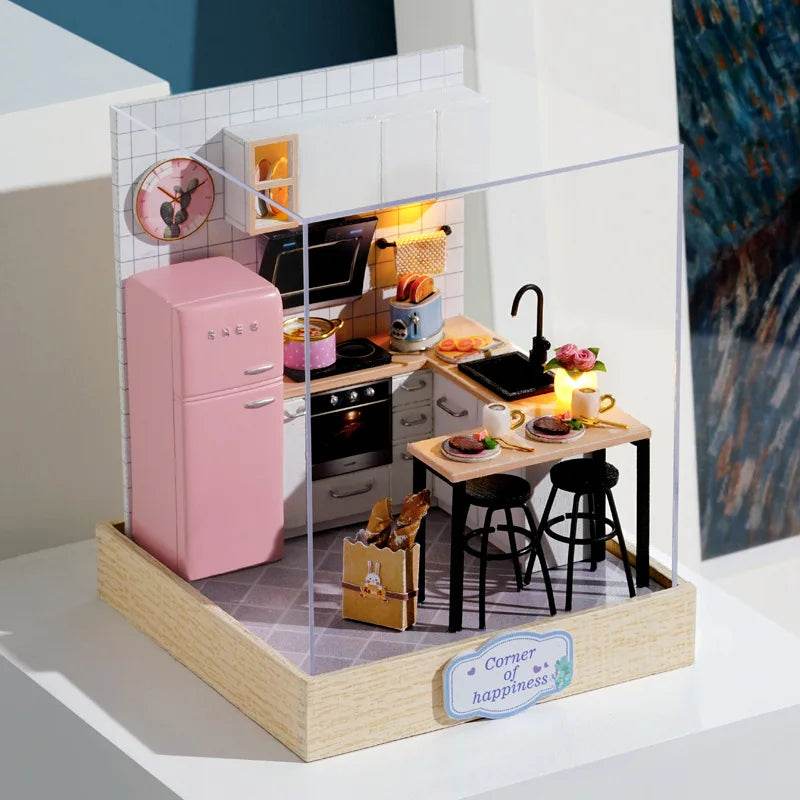 Miniature 3D flower house kit with pink fridge, black stools, wooden table, and kitchen appliances inside clear display case.