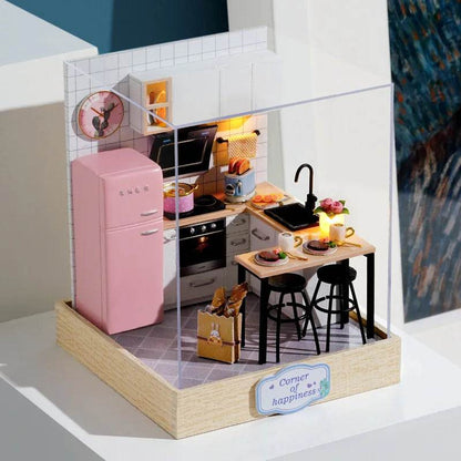 Miniature 3D flower house kit with pink fridge, black stools, wooden table, and kitchen appliances inside clear display case.