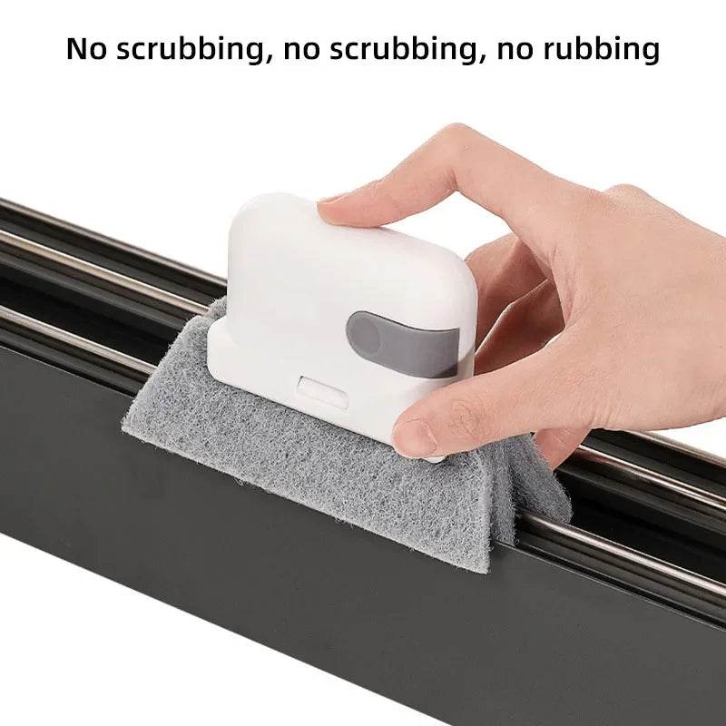 White hand-held crevice cleaning brush with gray grip and attached gray scrubber pad on black sliding door track.