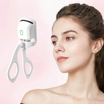 Compact white electric heated eyelash curler with silicone pad and ergonomic handles next to woman with natural makeup.