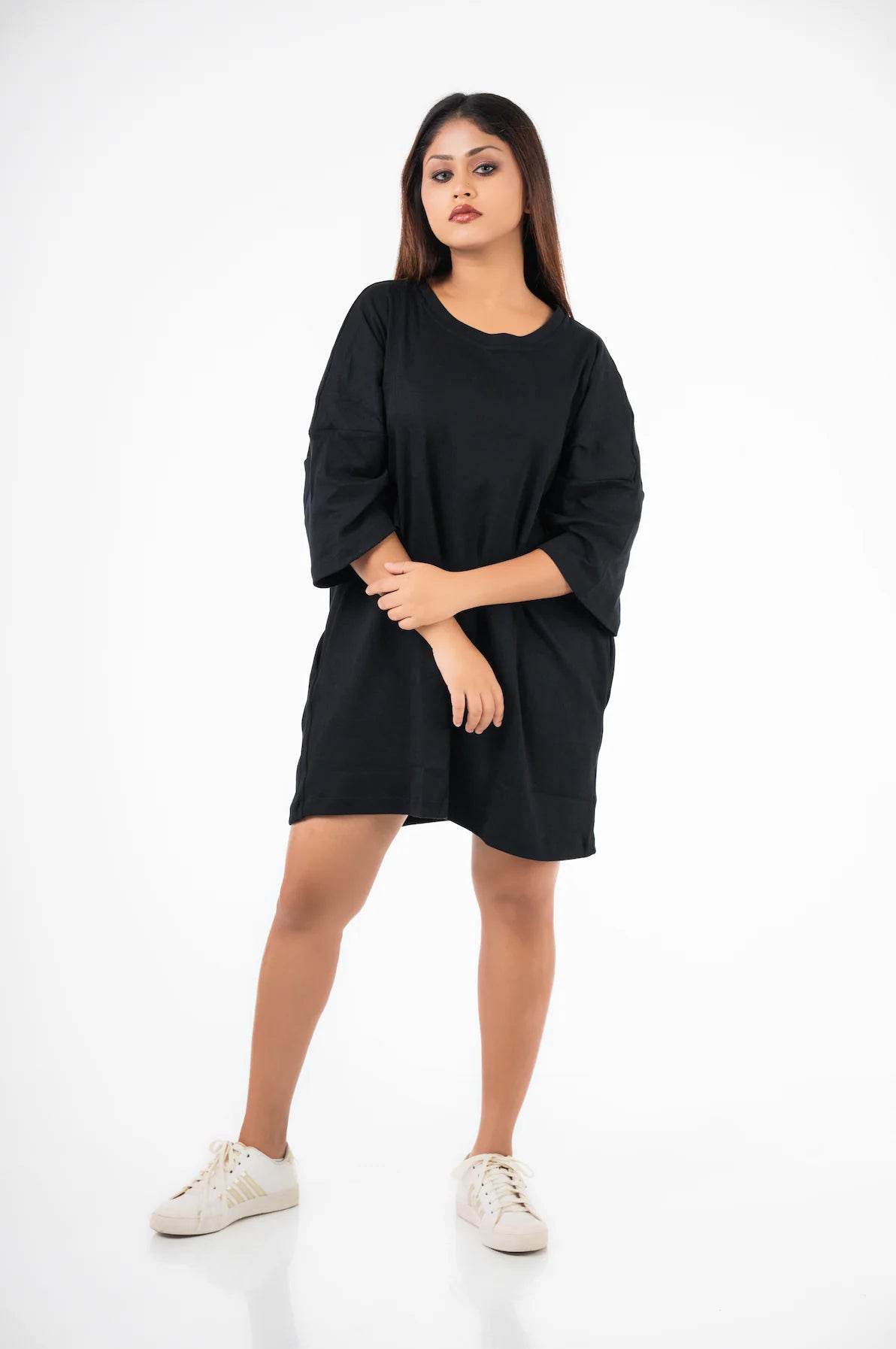 Relaxed fit black t-shirt dress with three-quarter sleeves worn with white sneakers.