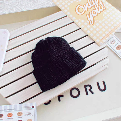Black knitted beanie hat for 17cm dolls on white slatted surface with decorative cards nearby.