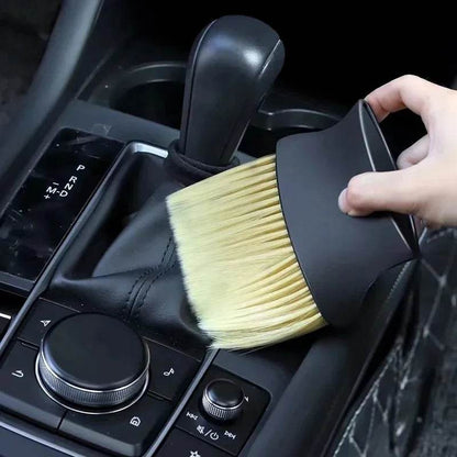 Soft yellow bristle dust brush with black handle cleaning car interior near gear shift and control knob.