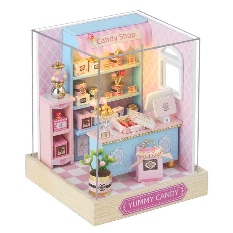 Miniature candy shop dollhouse with pastel pink and blue decor, shelves, sweets, and furniture on wooden base.