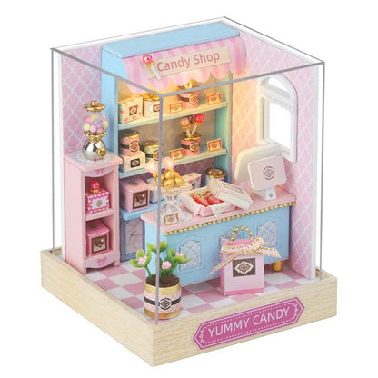 Miniature candy shop dollhouse with pastel pink and blue decor, shelves, sweets, and furniture on wooden base.