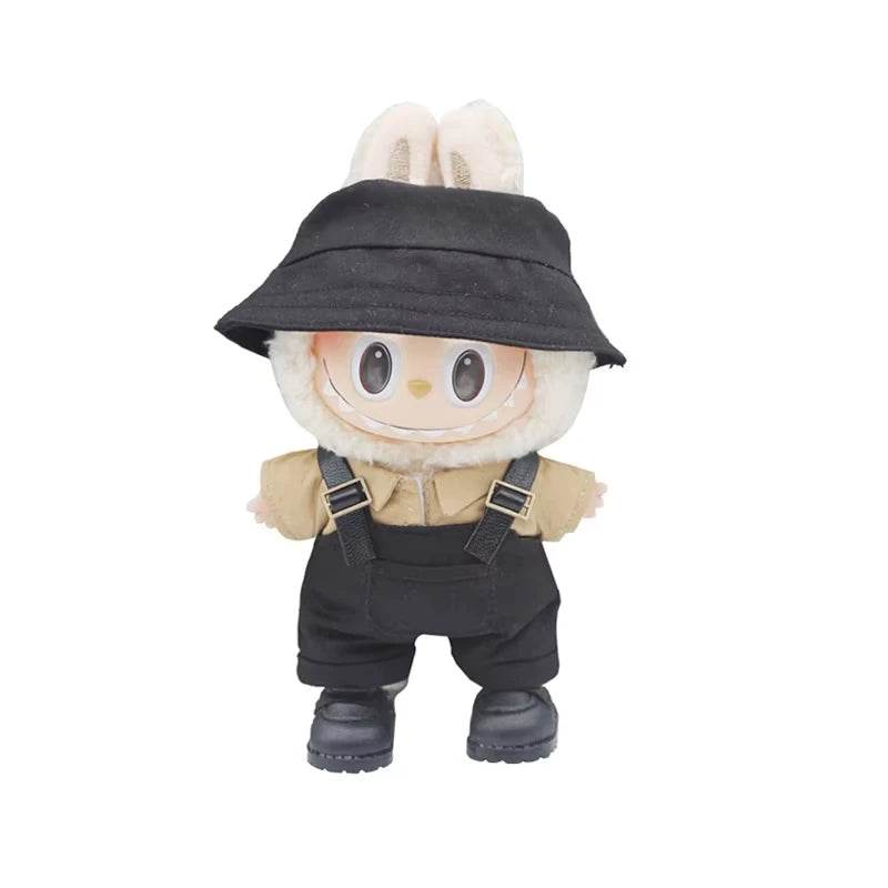 Small plush doll wearing beige bunny hat, black bucket hat, black striped overalls, and black shoes.