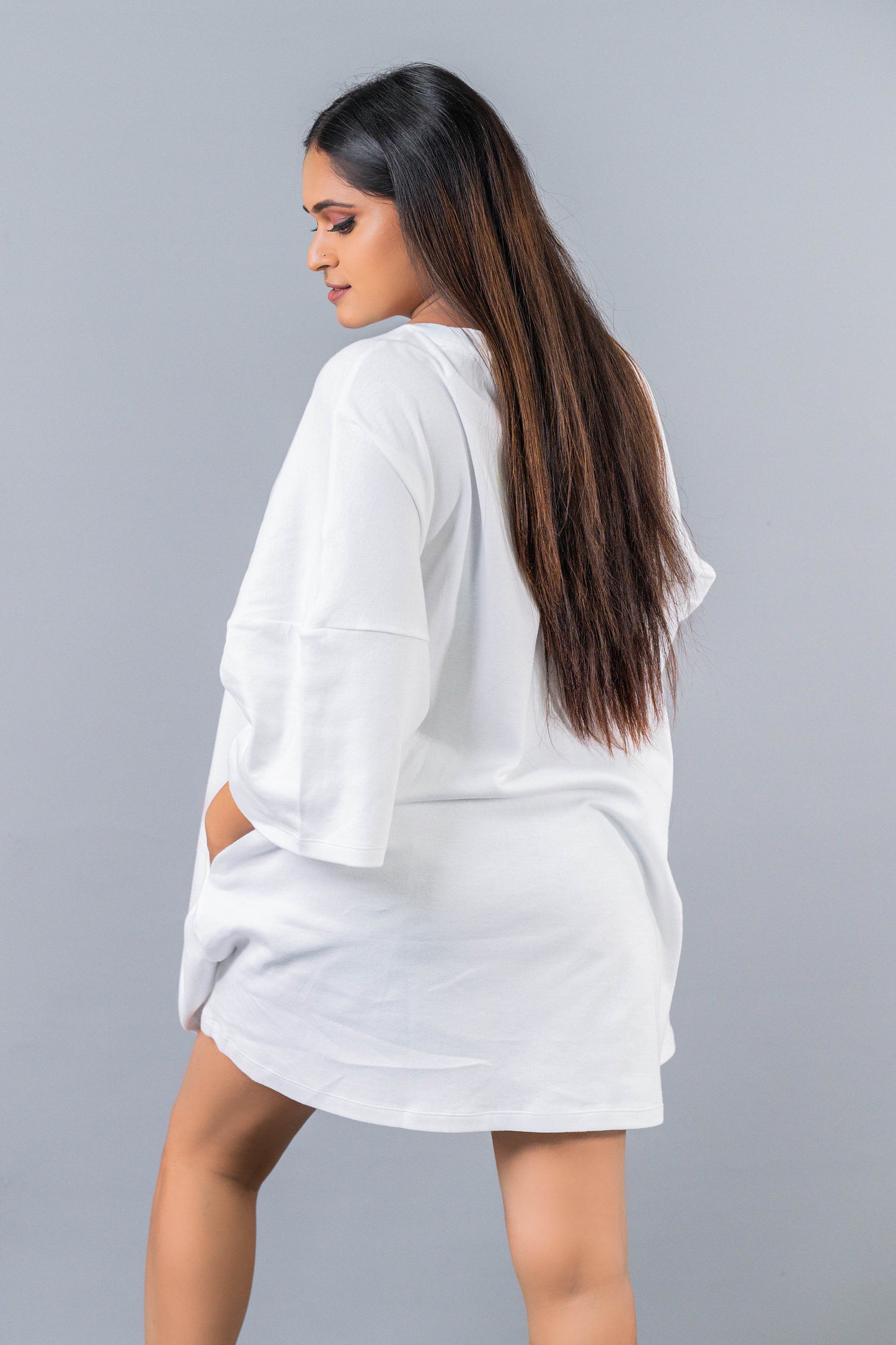 Relaxed fit white oversized T-shirt dress with elbow-length sleeves and side pockets, worn by a woman.
