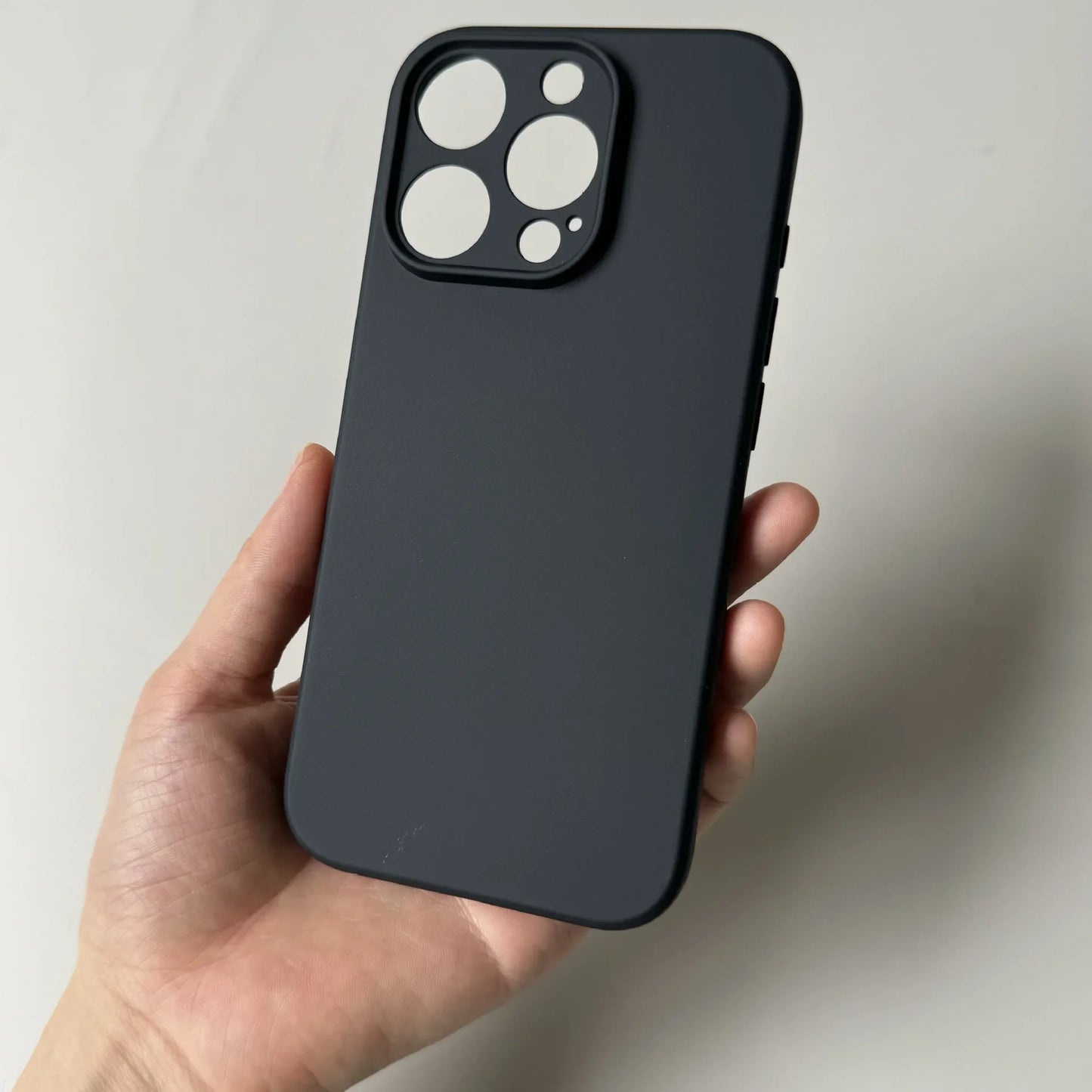 Black phone case held in a hand against a neutral background