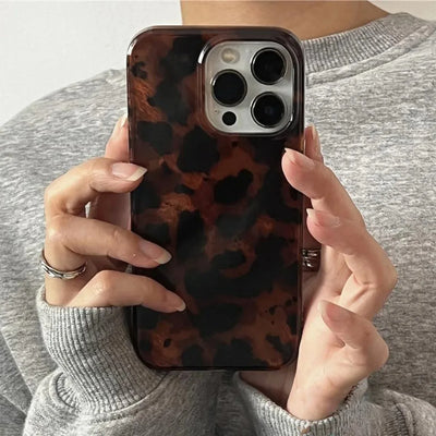 Person holding a phone with a leopard print case against a neutral background