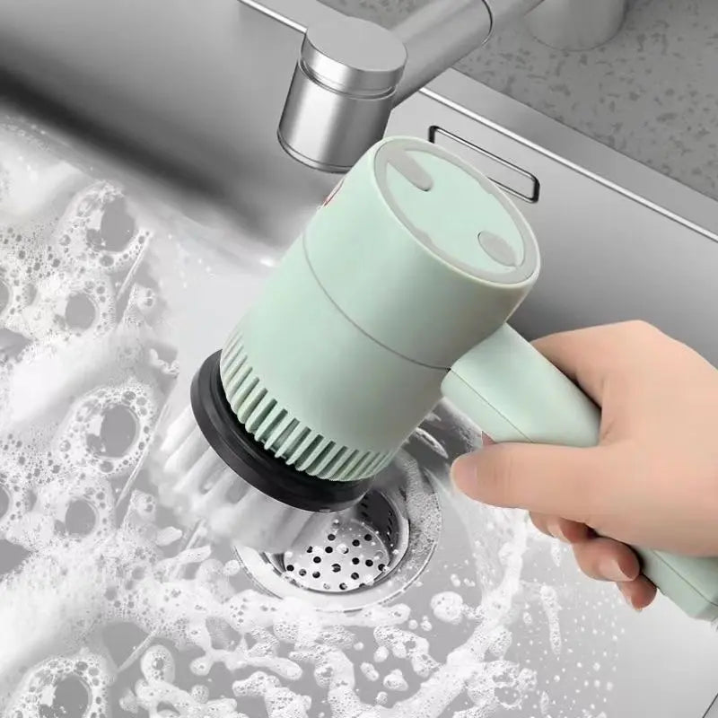 Hand using a green kitchen cleaning brush in a sink with soapy water.