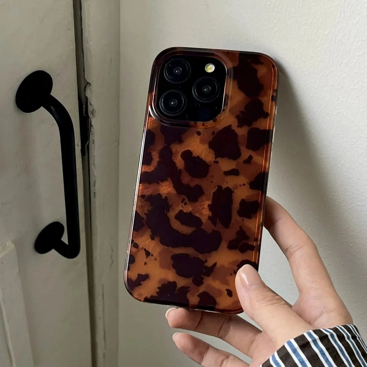 Hand holding a phone with a leopard print case against a neutral background