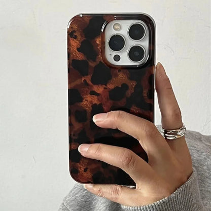 Hand holding a phone with a tortoiseshell case against a light background