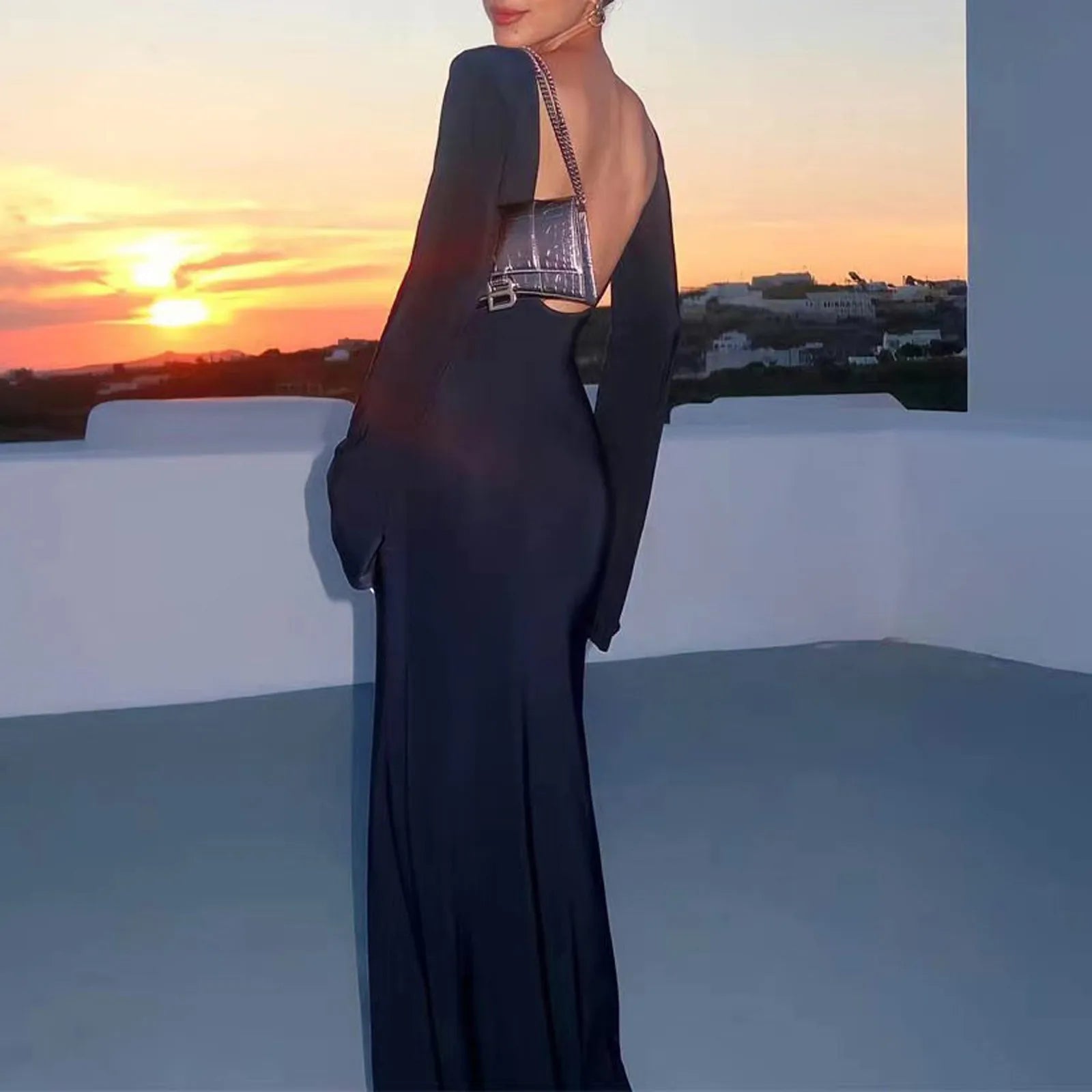 Woman in a black evening gown with a sunset and coastal view in the background