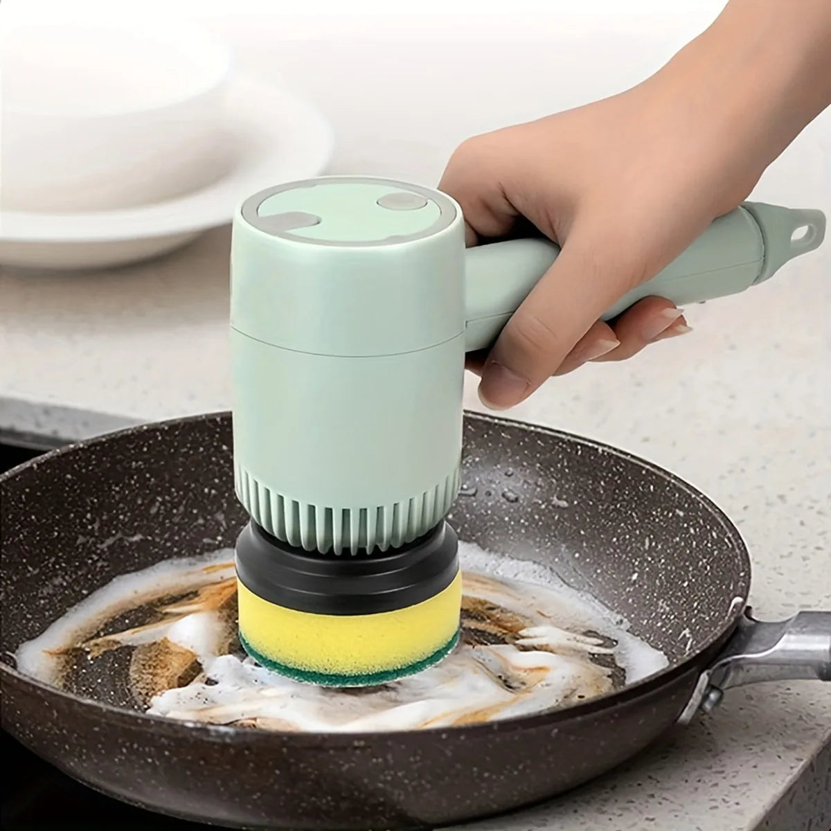Hand using a scrubber to clean a frying pan with soap suds.