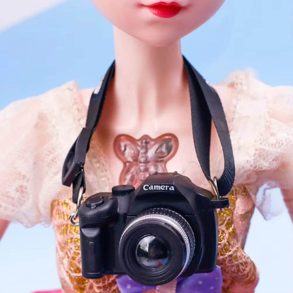 Black miniature DSLR camera necklace with strap on doll wearing yellow patterned dress.