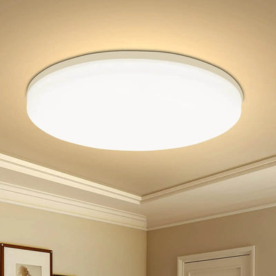 Round flush-mount LED ceiling light with white diffuser emitting warm white glow in beige room.