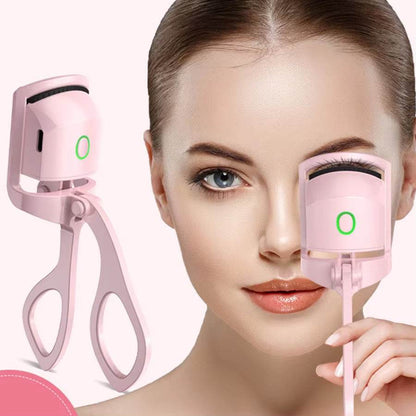 Pink rechargeable heated eyelash curler with ergonomic handle and glowing power button held near a woman's eye.