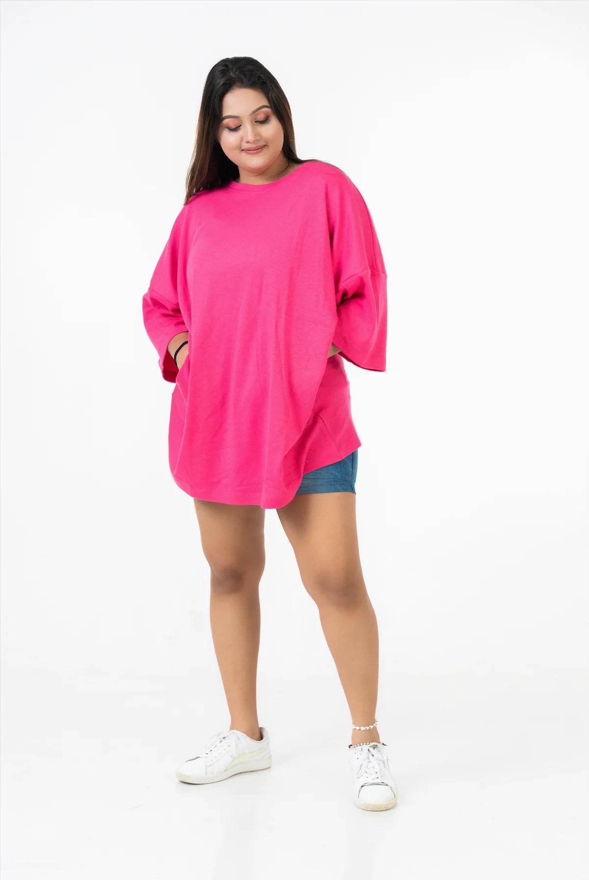 Bright pink relaxed fit oversized t-shirt with dropped shoulders worn with shorts and white sneakers.