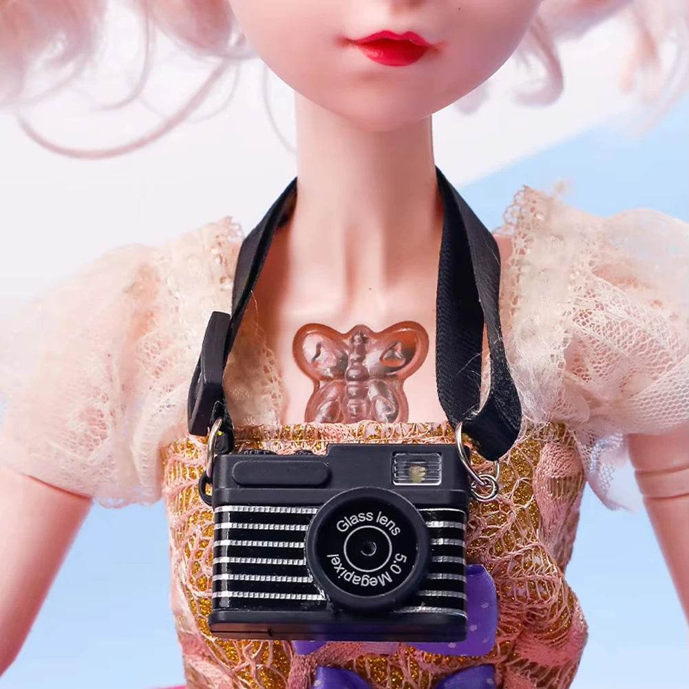Miniature black vintage-style camera necklace on doll wearing sheer puff sleeve dress with gold lace apron.
