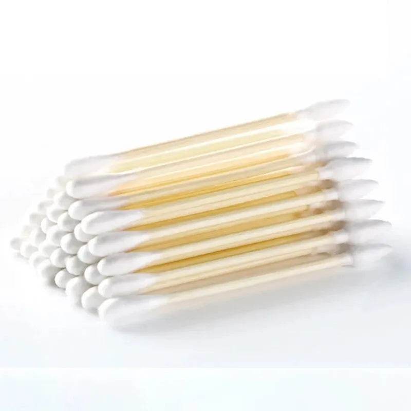 Stack of double-ended cotton swabs with wooden sticks and white round cotton tips on a white background.
