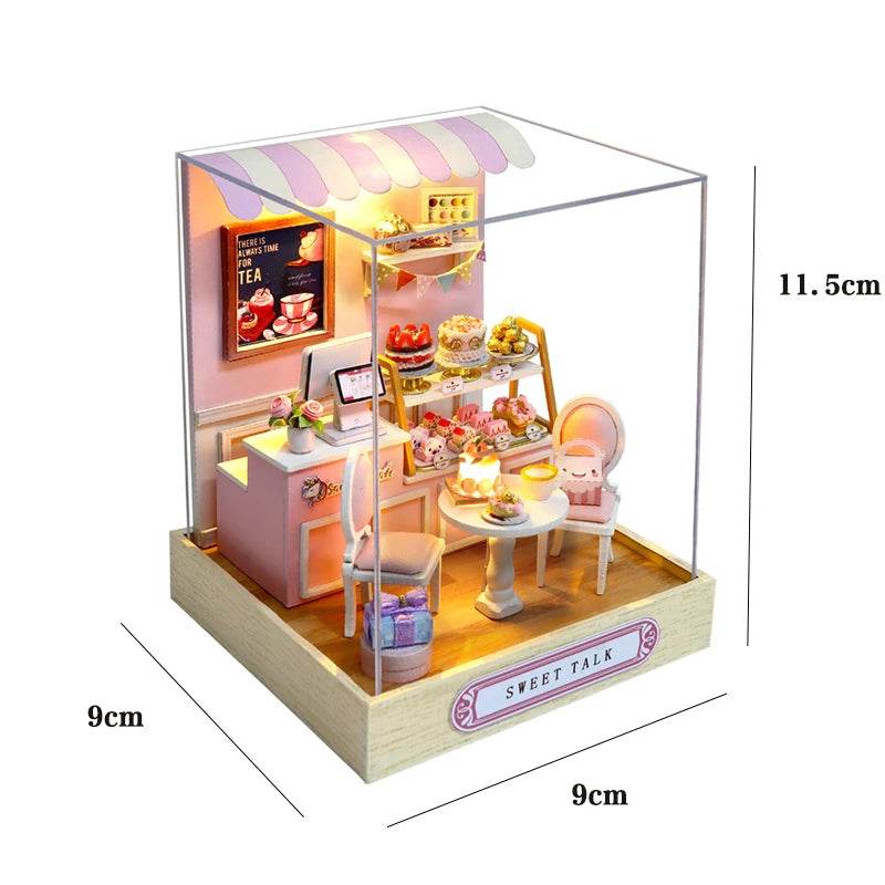 Miniature pastel pink and white flower-themed dollhouse cafe with table, chairs, counter, cakes, and striped canopy inside.