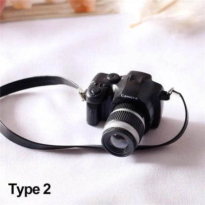 Black miniature DSLR camera toy with detailed lens and attached strap on white background.