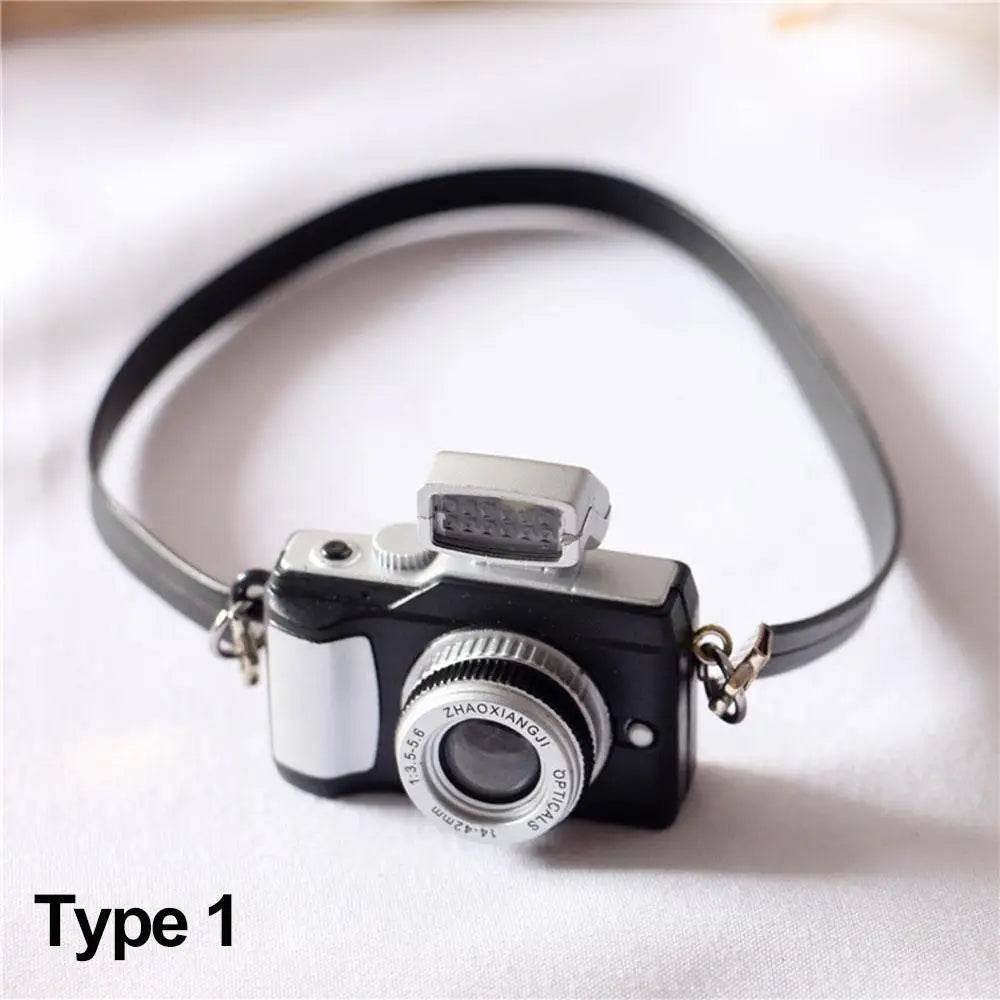 Black and silver miniature camera accessory with a gray strap for dolls.