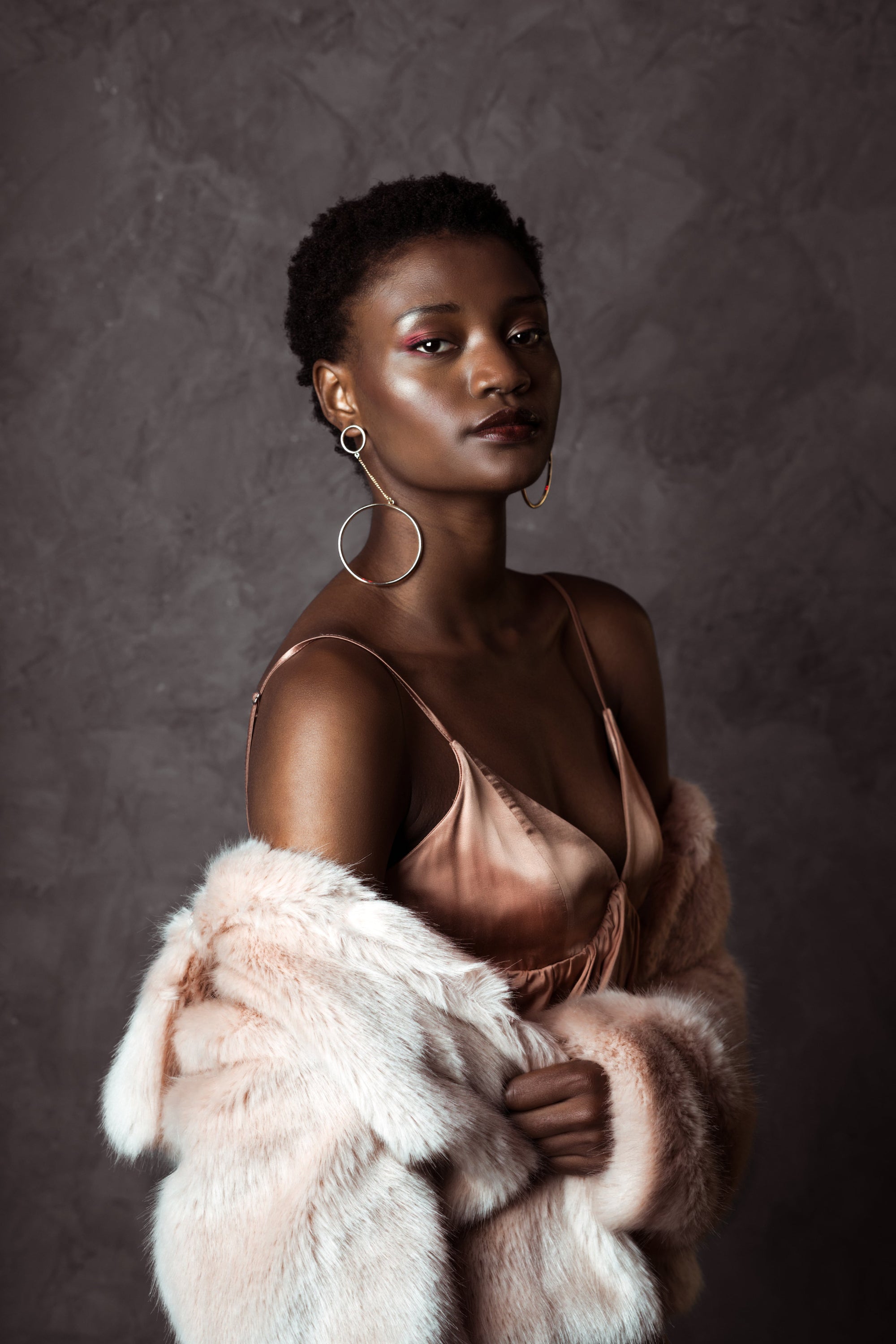 Woman in a brown dress holding a pink fur coat against a textured brown background